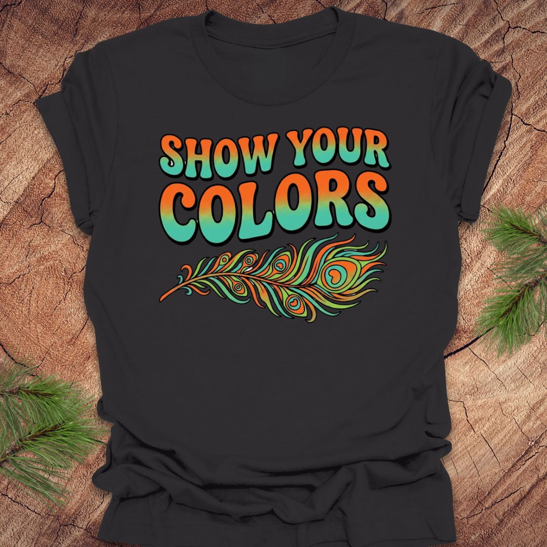 Dark gray t-shirt with 'Show Your Colors' text and peacock feather design on a wooden surface.