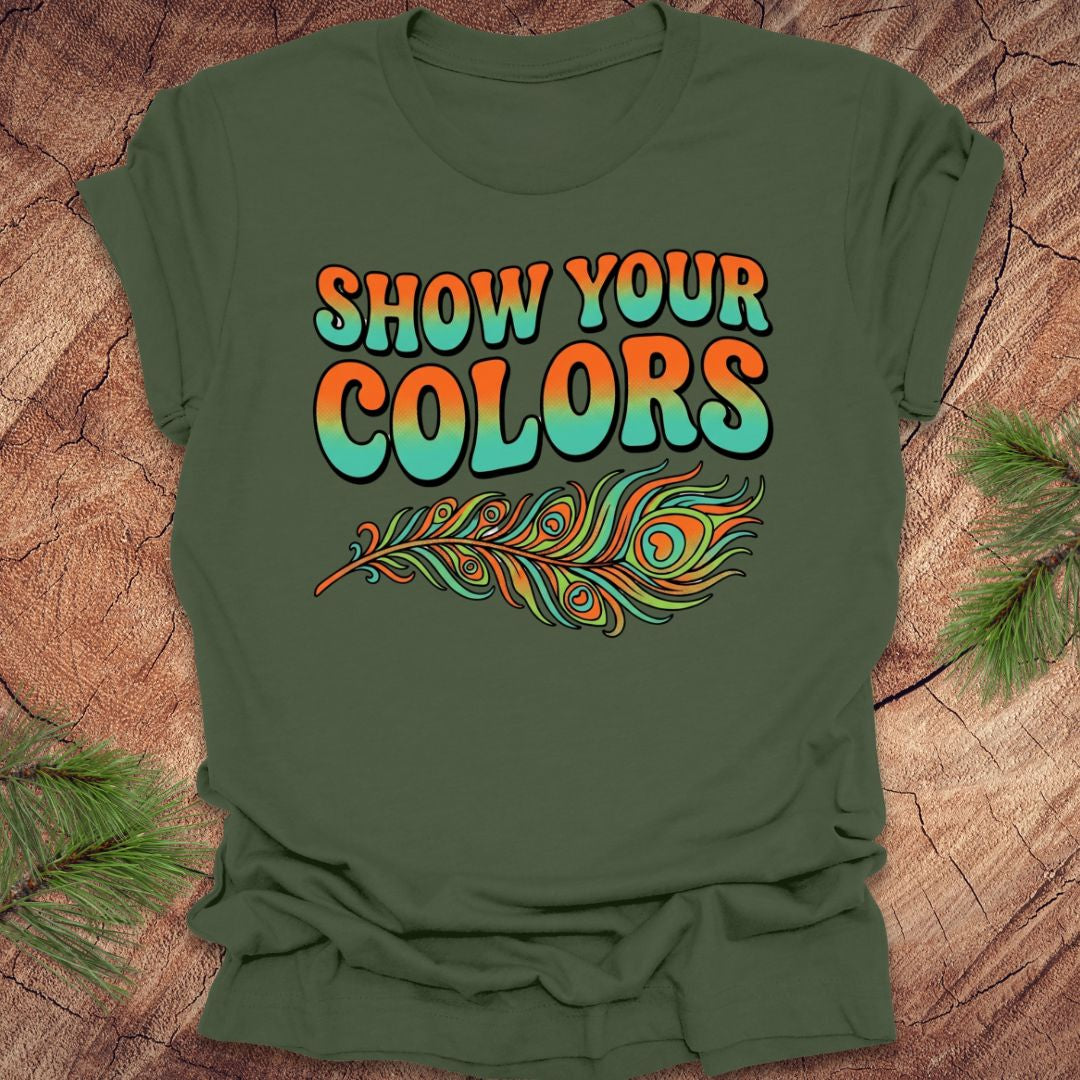 Green t-shirt with 'Show Your Colors' text and peacock feather design on a wooden surface.