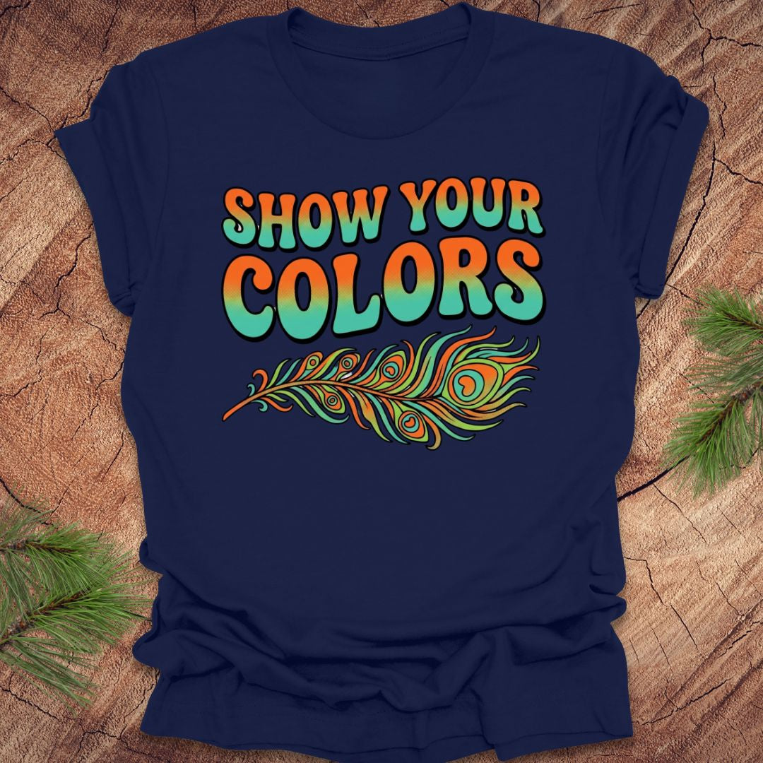 Navy blue t-shirt with 'Show Your Colors' text and peacock feather design on a wooden surface.