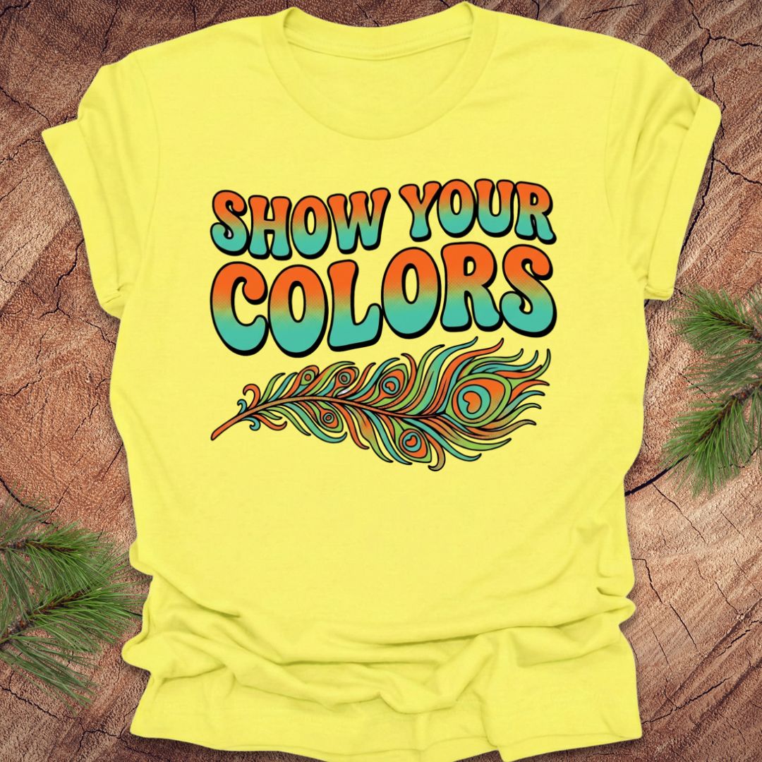 Yellow t-shirt with 'Show Your Colors' text and feather design on a wooden surface.