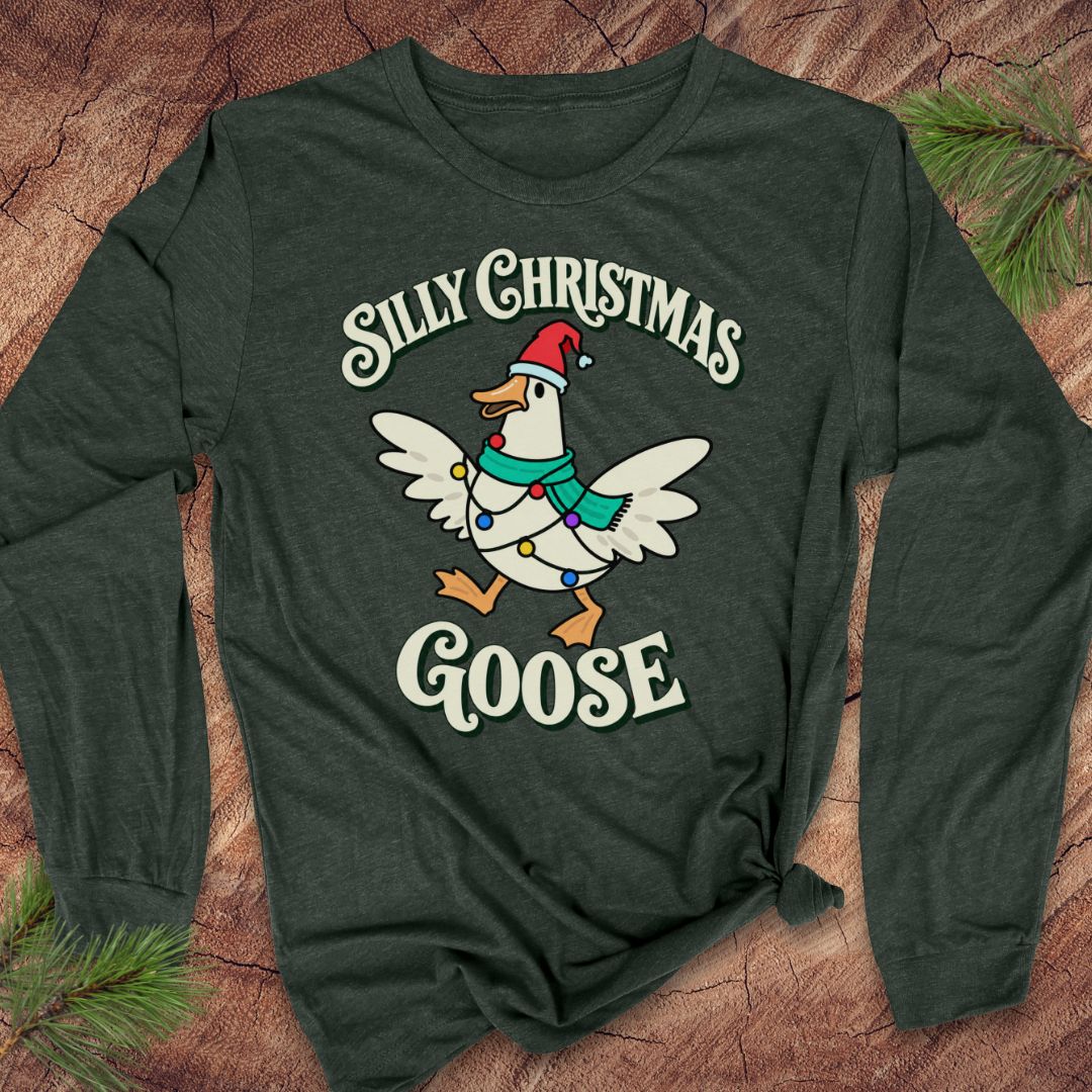 Heather forest green long-sleeve t-shirt with a goose in a Santa hat and teal scarf, wrapped in colorful Christmas lights under retro Silly Christmas Goose lettering, laid flat on a rustic wood background with pine branches.