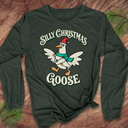 Heather forest green long-sleeve t-shirt with a goose in a Santa hat and teal scarf, wrapped in colorful Christmas lights under retro Silly Christmas Goose lettering, laid flat on a rustic wood background with pine branches.