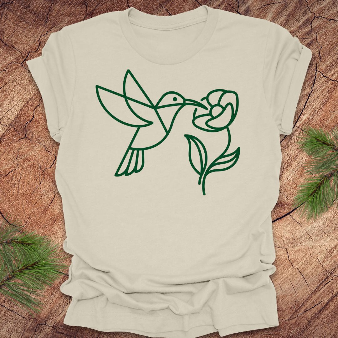 Beige t-shirt with green line art of a hummingbird and flower on a wooden surface.