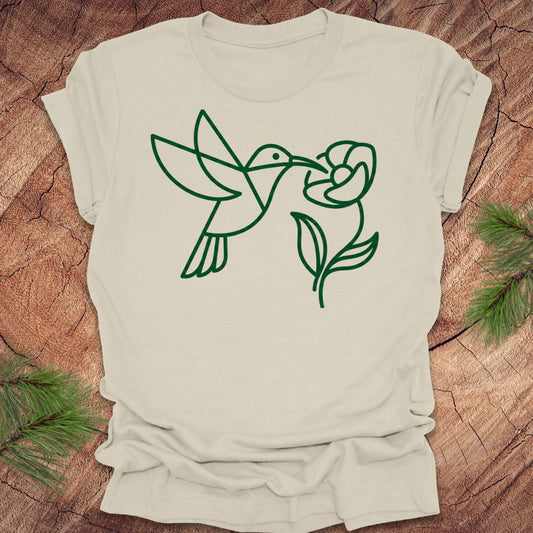 Beige t-shirt with green line art of a hummingbird and flower on a wooden surface.