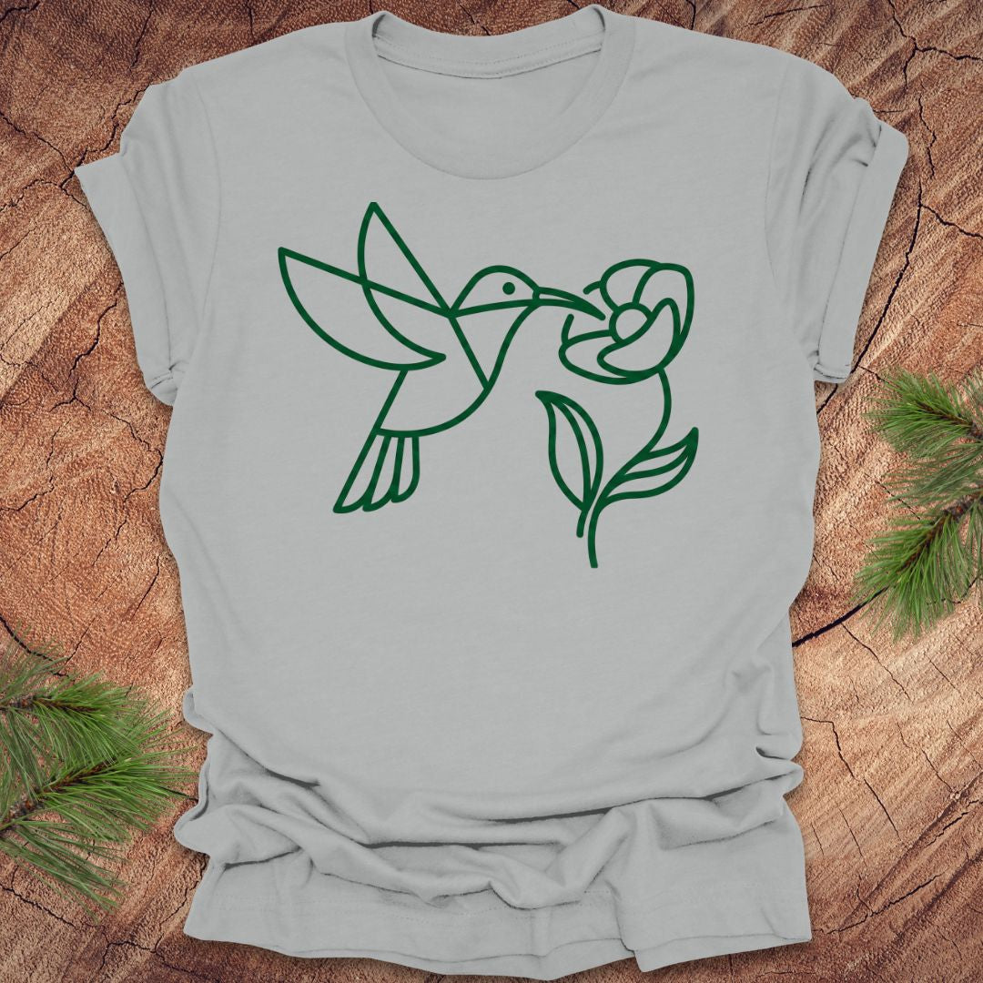 Gray t-shirt with green line art of a hummingbird and flower on a wooden surface.