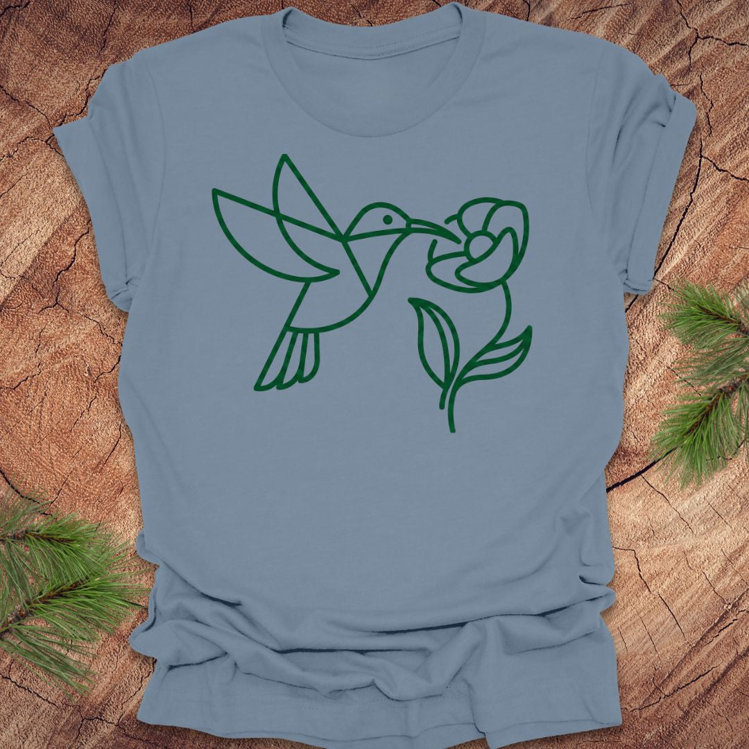 Blue t-shirt with green line art of a hummingbird and flower on a wooden surface.