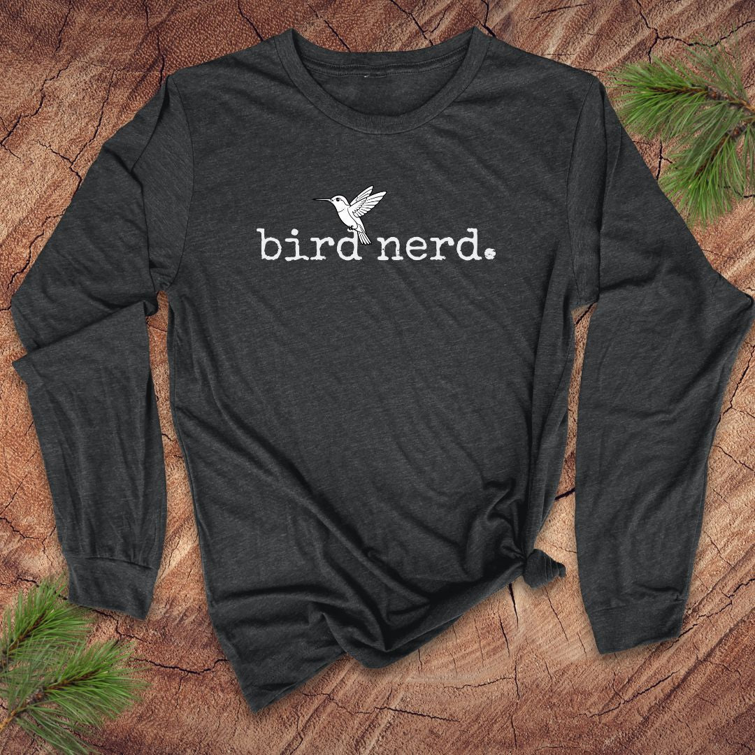 Dark long-sleeve shirt with 'bird nerd' text and bird graphic on a wooden surface with pine branches.