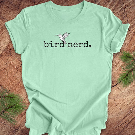 Mint green t-shirt with 'bird nerd' text and a hummingbird graphic on a wooden surface.