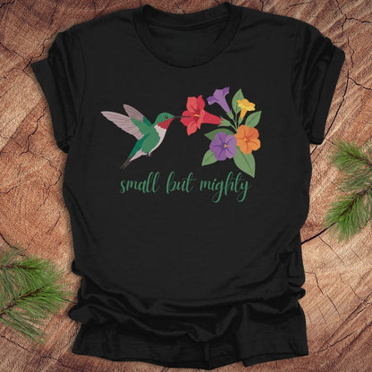 Black t-shirt with a hummingbird and flowers with text, 'small but mighty' on a wooden surface