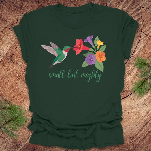 Green t-shirt with a hummingbird and flowers with text, 'small but mighty' on a wooden surface