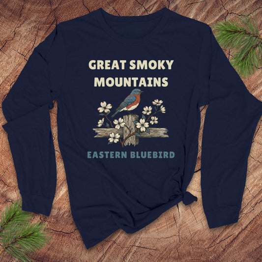 Navy blue long-sleeve tshirt with 'Great Smoky Mountains' and 'Eastern Bluebird' text on a wooden surface with pine branches.
