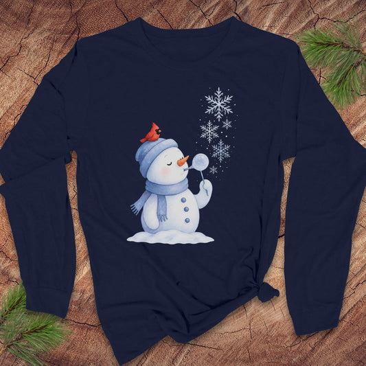 A navy blue long-sleeve t-shirt with a winter snowman graphic, laid flat on a rustic wood background with pine needles.