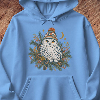 Carolina blue hoodie with a Snowy Owl in an orange pom-pom knit beanie, nestled in pine boughs, pinecones, and red berries under a crescent moon, laid flat on a rustic wood background.