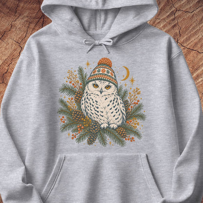 Sport grey hoodie with a Snowy Owl in an orange pom-pom knit beanie, nestled in pine boughs, pinecones, and red berries under a crescent moon, laid flat on a rustic wood background.