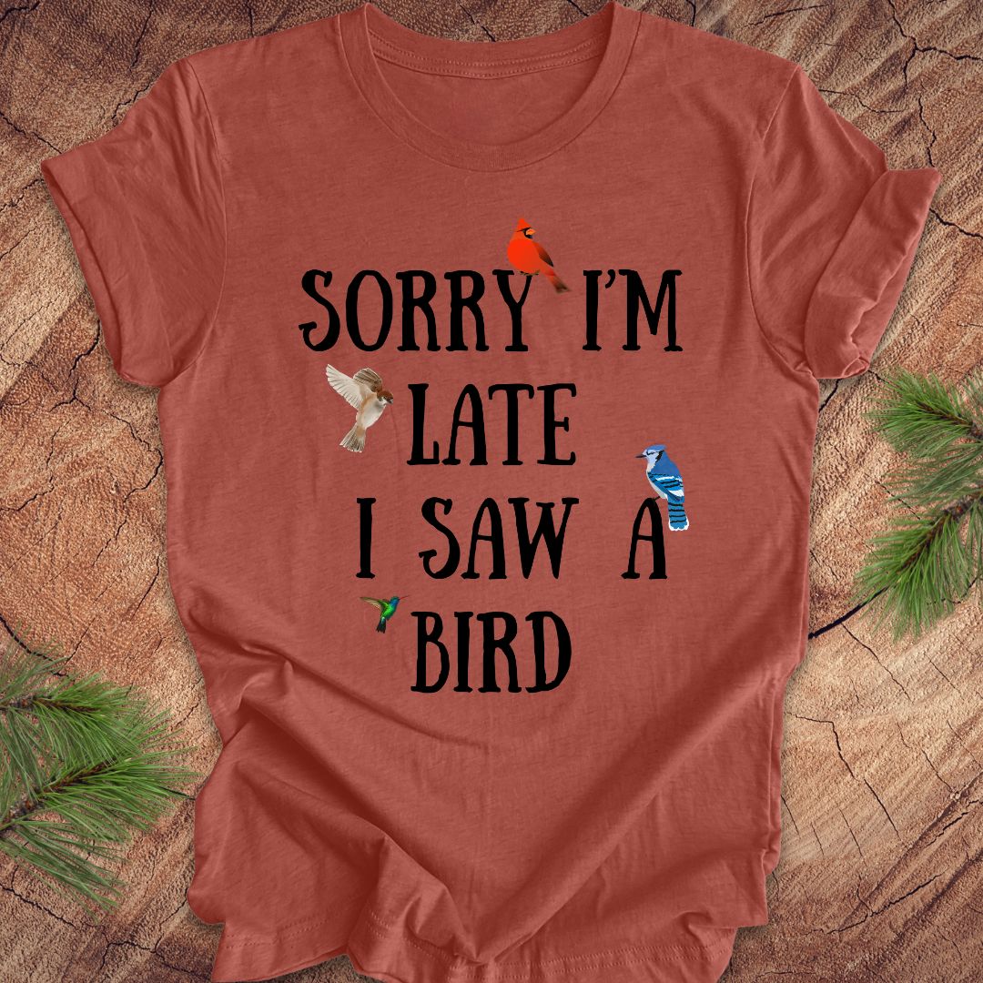 Red t-shirt with text 'Sorry I'm late I saw a bird' on a wooden surface.