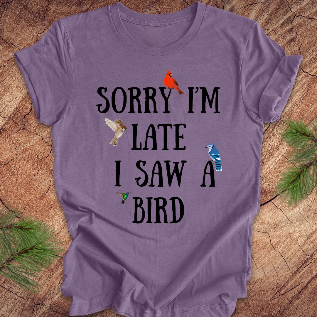 Purple t-shirt with text 'Sorry I'm late I saw a bird' on a wooden surface.