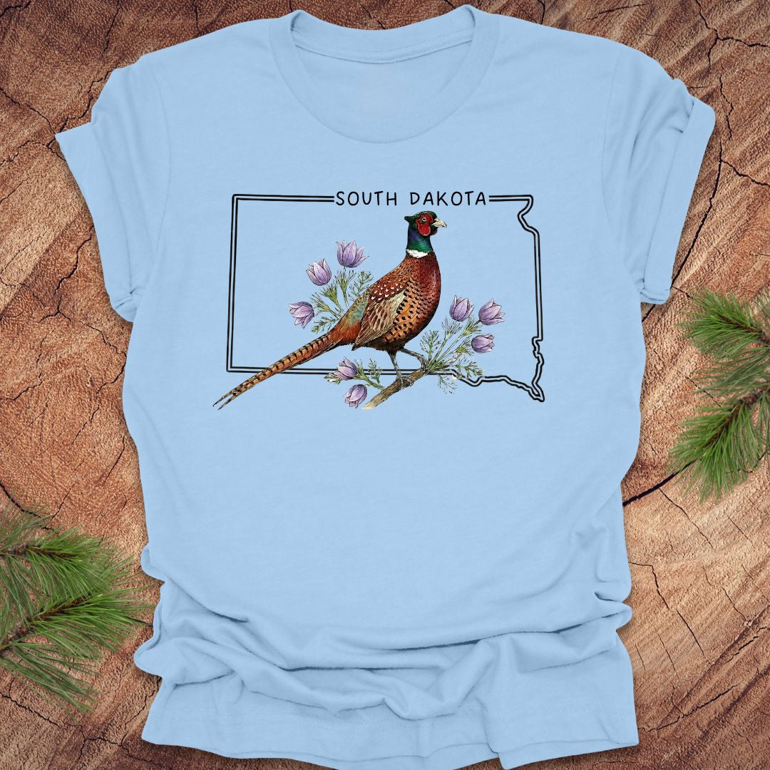 Light blue t-shirt with a pheasant and South Dakota outline design on a wooden surface.