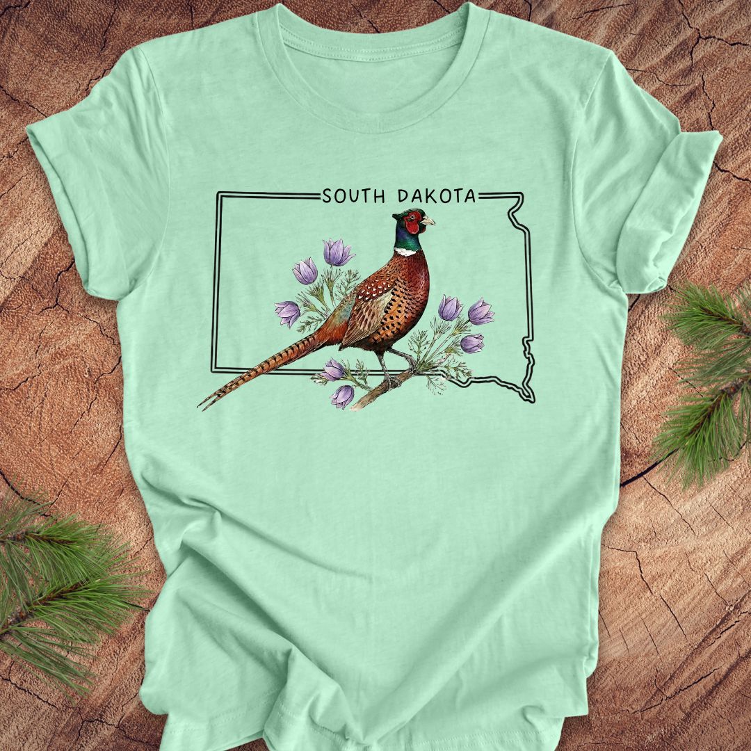 Mint green t-shirt with a pheasant and South Dakota outline design on a wooden surface.