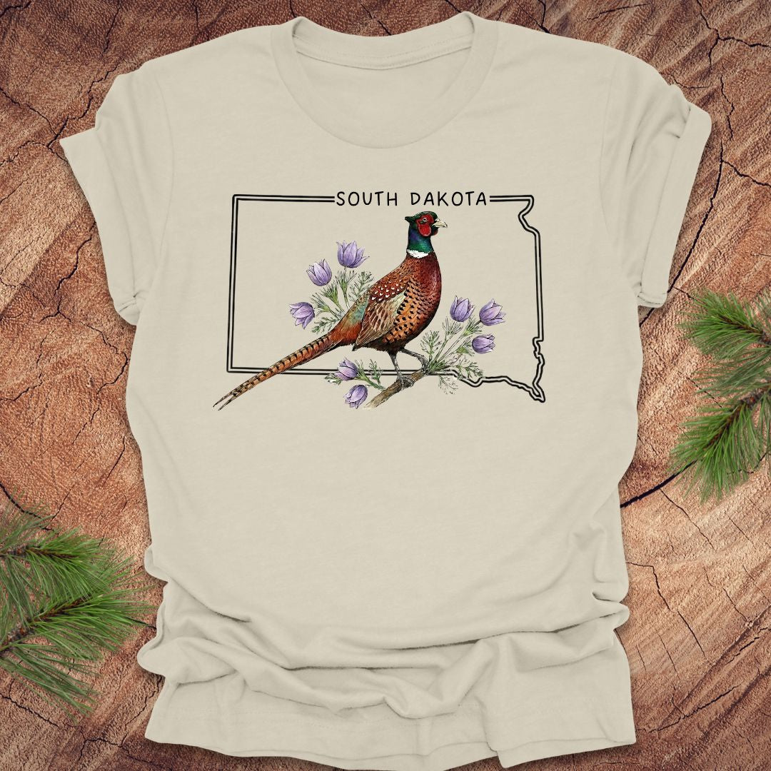 Beige t-shirt with a pheasant and South Dakota outline design on a wooden surface.