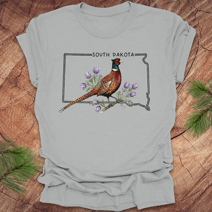 Gray t-shirt with a pheasant and South Dakota outline design on a wooden surface.