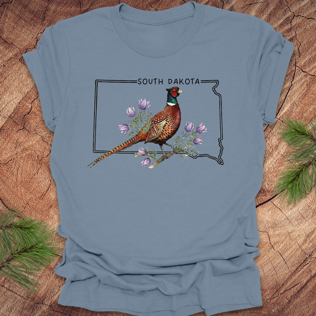 Blue t-shirt with a pheasant and South Dakota outline design on a wooden surface.