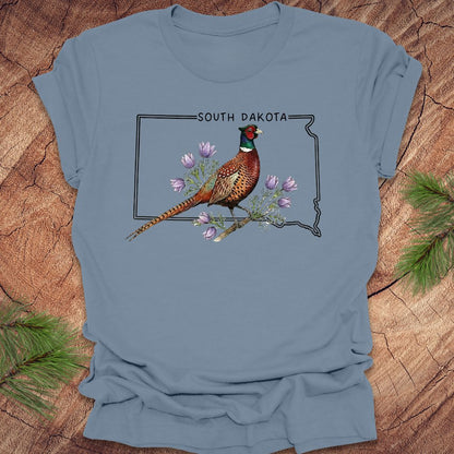 Blue t-shirt with a pheasant and South Dakota outline design on a wooden surface.