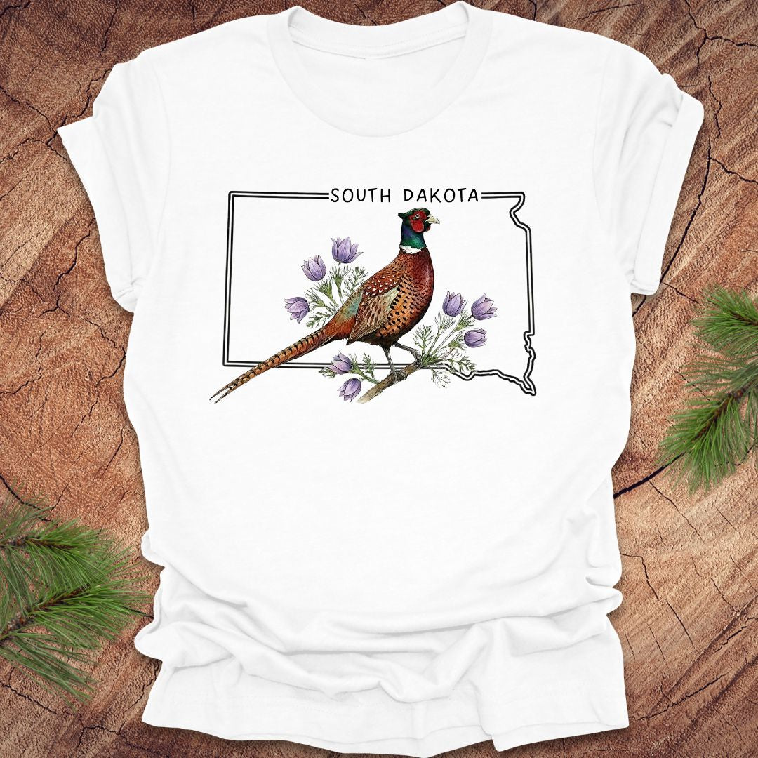 White t-shirt with a pheasant and South Dakota outline design on a wooden surface.
