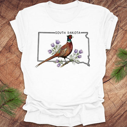 White t-shirt with a pheasant and South Dakota outline design on a wooden surface.