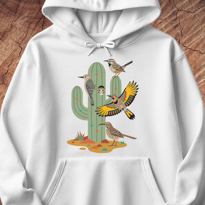 A white pullover hoodie featuring a colorful graphic print of desert birds perched on and around a saguaro cactus, displayed against a rustic brown wood background.