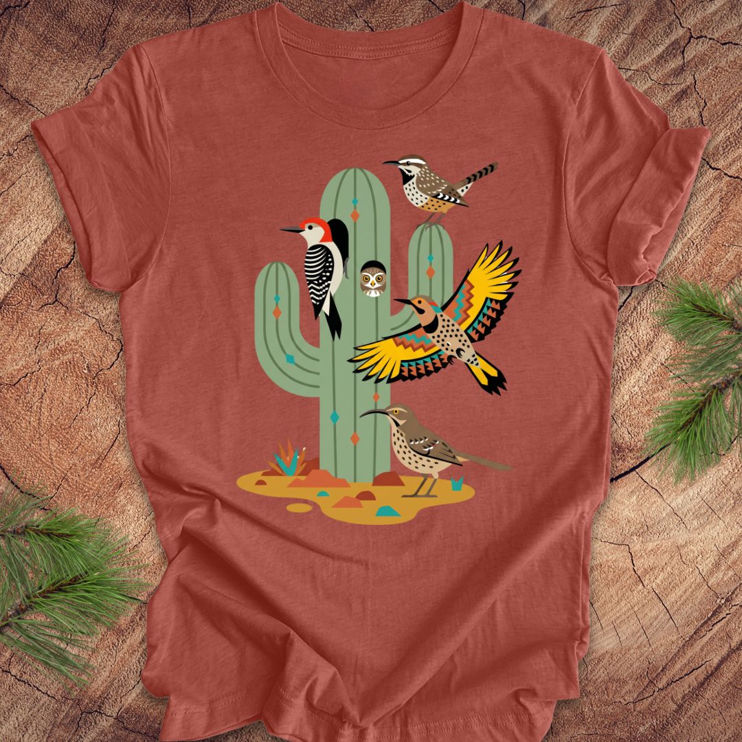 Clay colored t-shirt with a cactus and birds design on a wooden surface