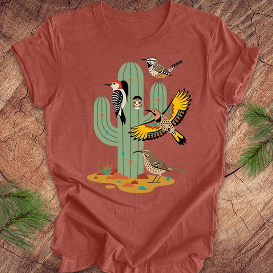 Clay colored t-shirt with a cactus and birds design on a wooden surface