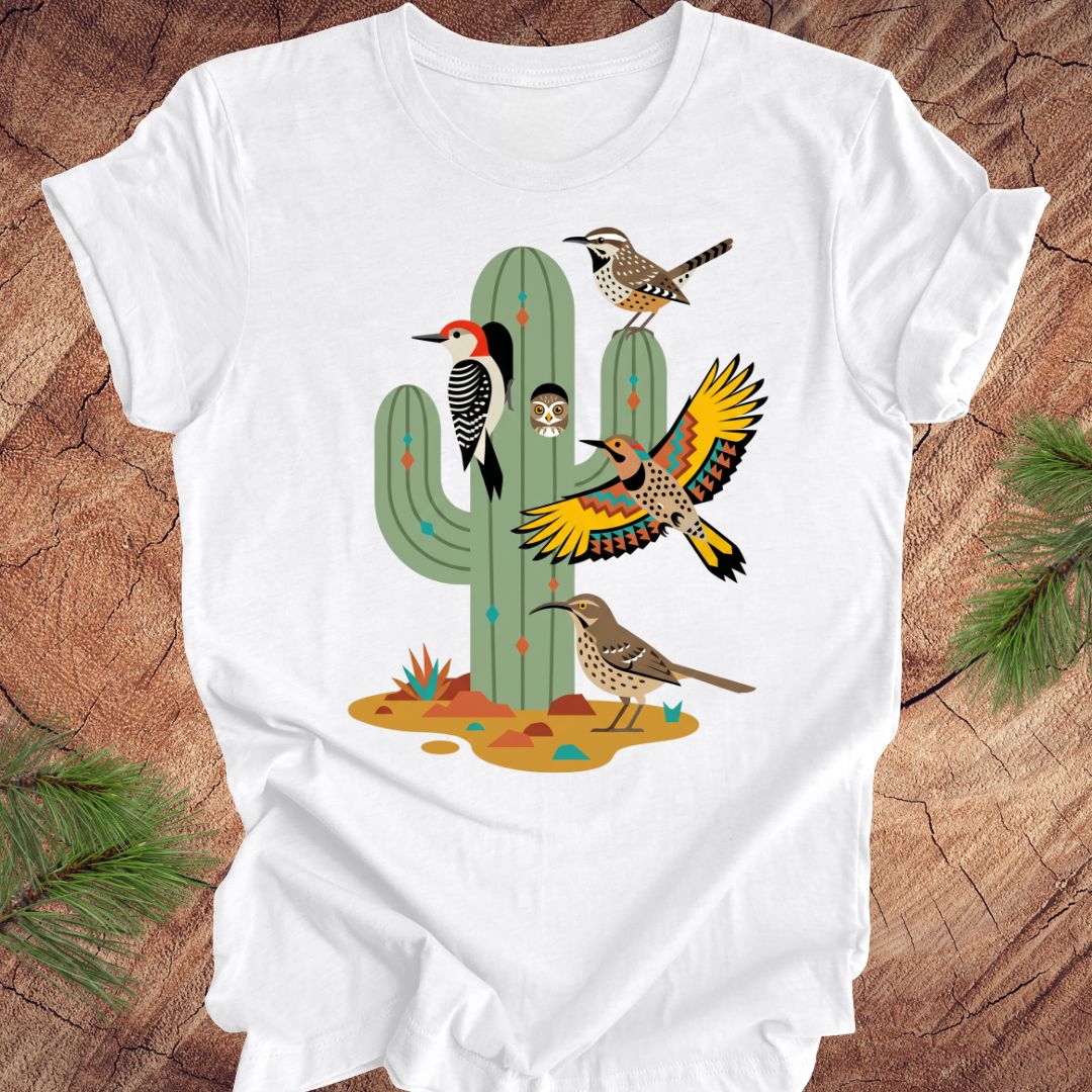 White t-shirt with a colorful cactus and birds design on a wooden surface.