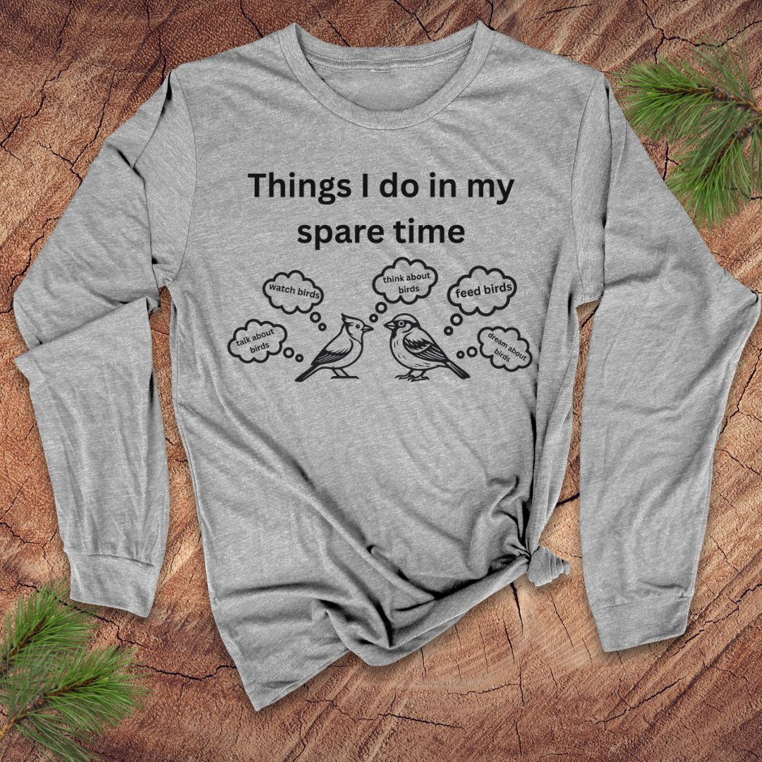 Gray long-sleeve tshirt with white text 'things i do in my spare time' with bird graphic and thought bubbles, on a wood surface.