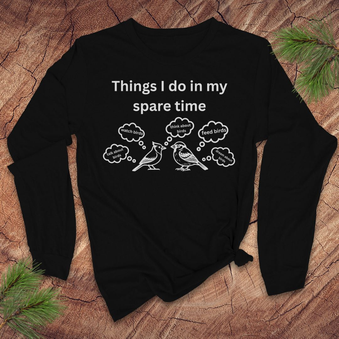 Black long-sleeve tshirt with white text 'things i do in my spare time' with bird graphic and thought bubbles, on a wood surface.