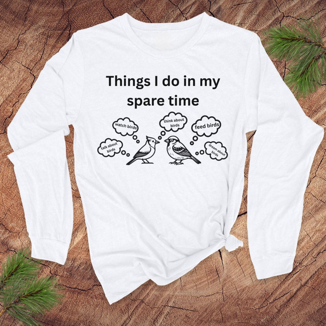 White long-sleeve tshirt with white text 'things i do in my spare time' with bird graphic and thought bubbles, on a wood surface.