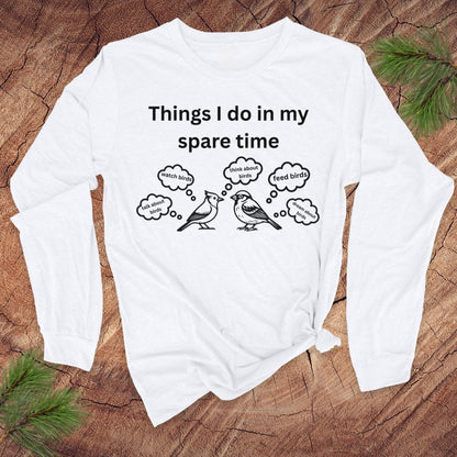 White long-sleeve tshirt with white text 'things i do in my spare time' with bird graphic and thought bubbles, on a wood surface.