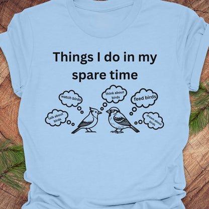 Light blue t-shirt with black text and bird illustrations on a wooden surface