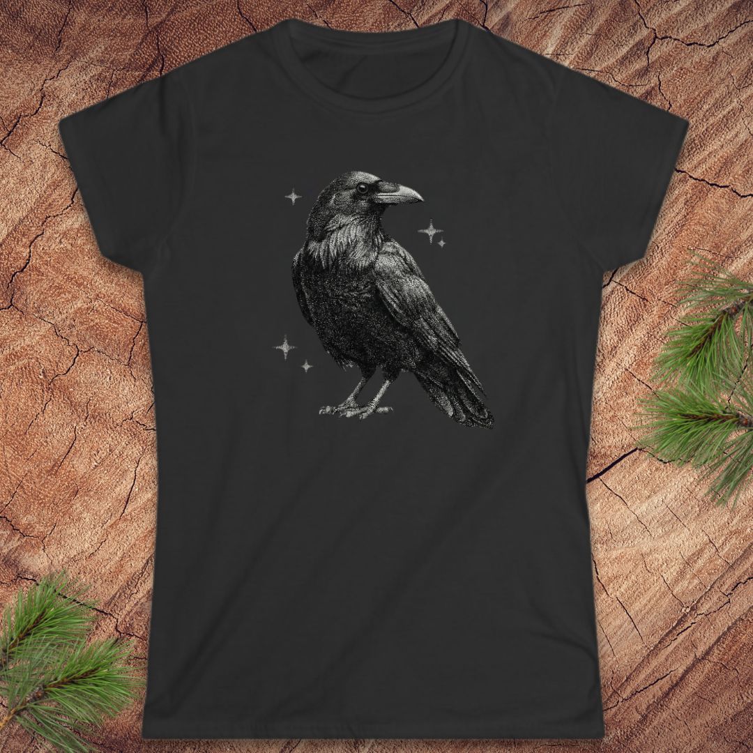 Black t-shirt with a raven design on a wooden surface with pine branches.
