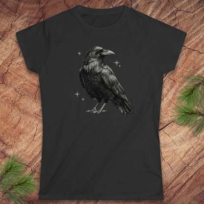 Black t-shirt with a raven design on a wooden surface with pine branches.