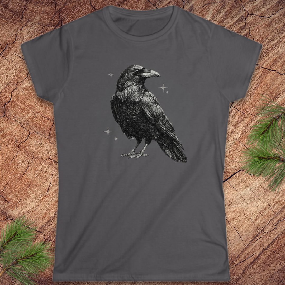 Gray t-shirt with a raveb design on a wooden surface with pine branches.
