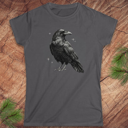 Gray t-shirt with a raveb design on a wooden surface with pine branches.