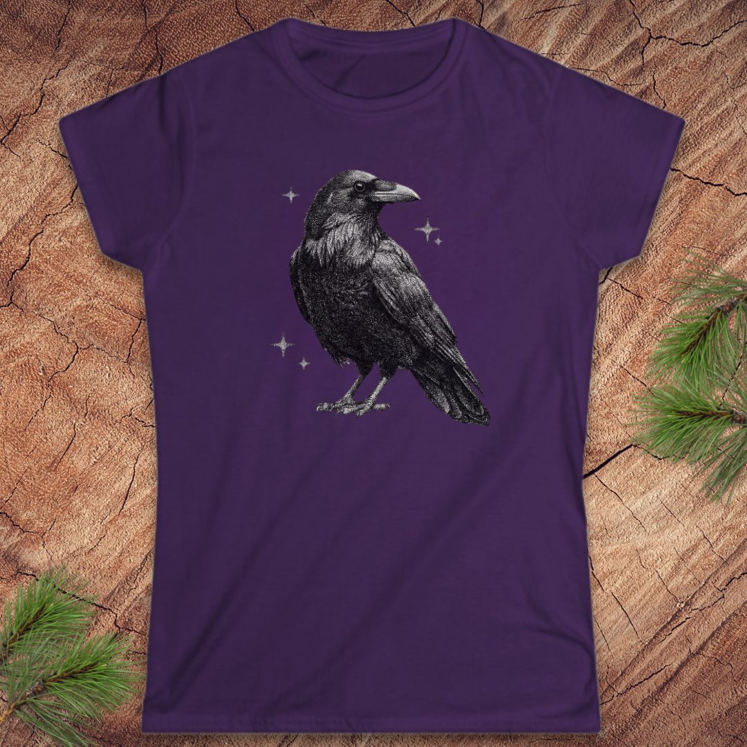 Purple t-shirt with a raveb design on a wooden surface with pine branches.