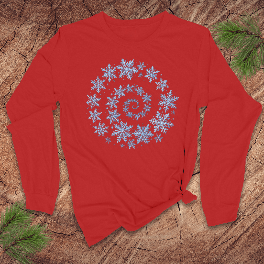 Red long sleeve shirt with a blue snowflake spiral design on a wooden surface with pine branches.