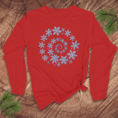 Red long sleeve shirt with a blue snowflake spiral design on a wooden surface with pine branches.
