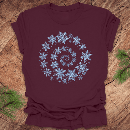 Maroon t-shirt with a spiral pattern of snowflakes on a wooden surface.