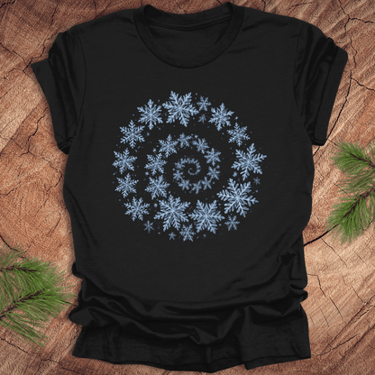 Black t-shirt with a spiral pattern of snowflakes on a wooden surface.