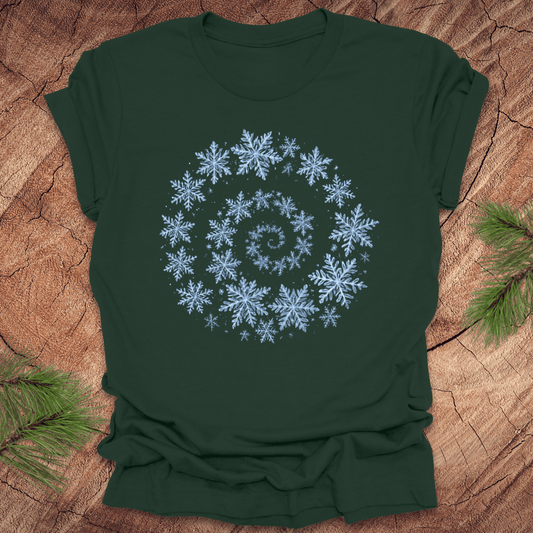 Green t-shirt with a spiral pattern of snowflakes on a wooden surface.