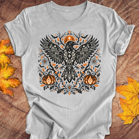 A gray heather t-shirt with a folk art crow and pumpkin halloween design on a wood background with fall leaves. 
