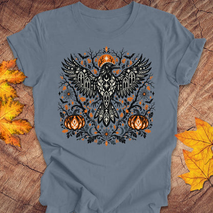 A steel blue t-shirt with a folk art crow and pumpkin halloween design on a wood background with fall leaves. 