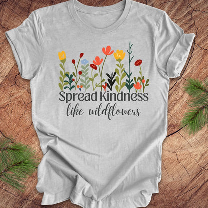 Gray t-shirt with floral design and 'Spread Kindness like wildflowers' text on a wooden surface.